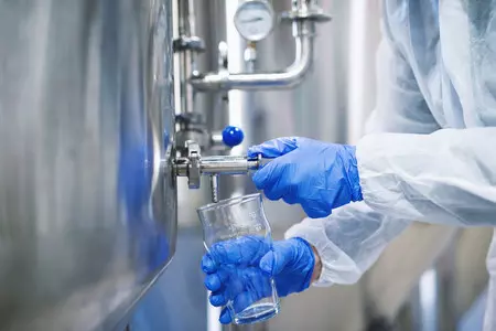 clanki/close-up-view-hands-protective-gloves-opening-tap-valve-filling-glass-with-samples-